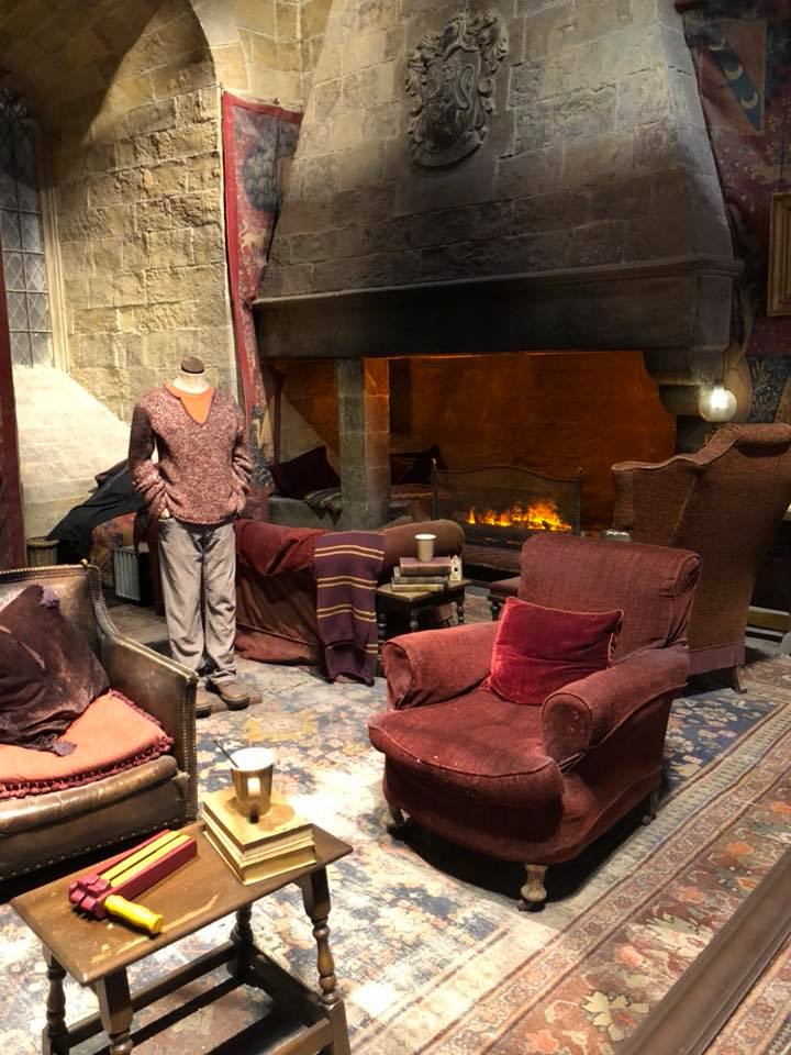 Photo shows the set of the Gryffindor common room with red arm chair and a roaring fire place in the background.