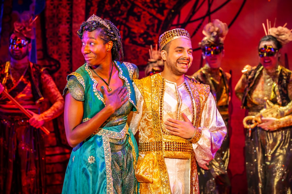 Aladdin, wearing a golden and white hasten clothing, smiling holding Jasmine, who is wearing a green hasten costume.