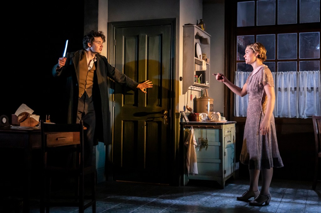 Photo shows Alice (Jessie Hills) and Ian Tracey (Patrick Walshe McBride) in the back kitchen having a heated confrontation, with Ian Tracey holding a bread knife in a threatening way, whilst keeping th door to the upstairs rooms shut.