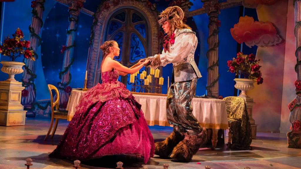 Photo shows both and the best dancing in the dining hall, bell is wearing a dark purple ball dress, and the best a bear like creature with horns on his head is wearing a while shirt in blue and grey trousers with masssive brown hooves.