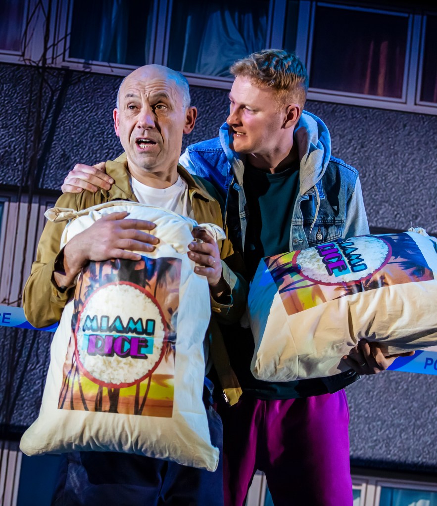 Photo shows Jack and Lewis holding sacks of rice. with lewis talking to Jack with Jack having a worried look on his face.