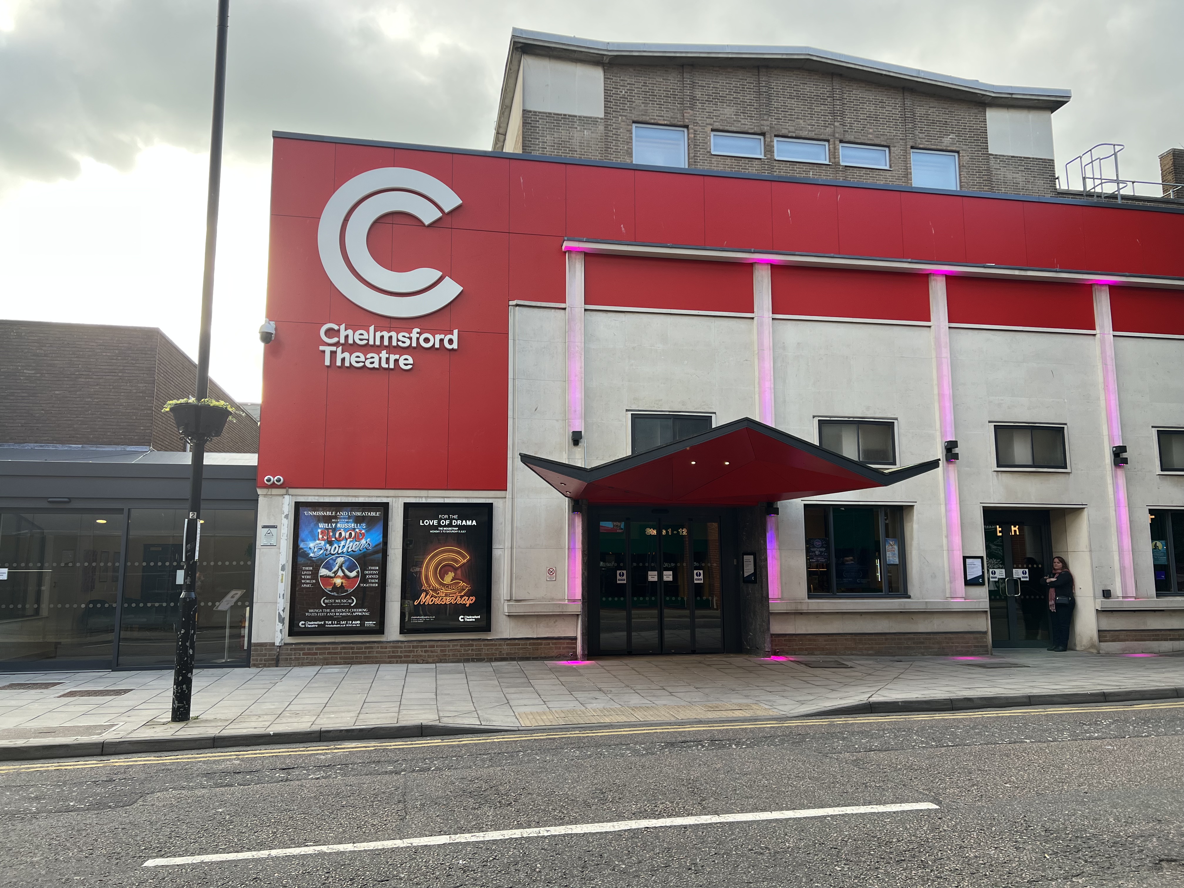A outside shot of the Chelmsford theatre with a red coloured top half with the lego in white. with pink lights going down the walls.
