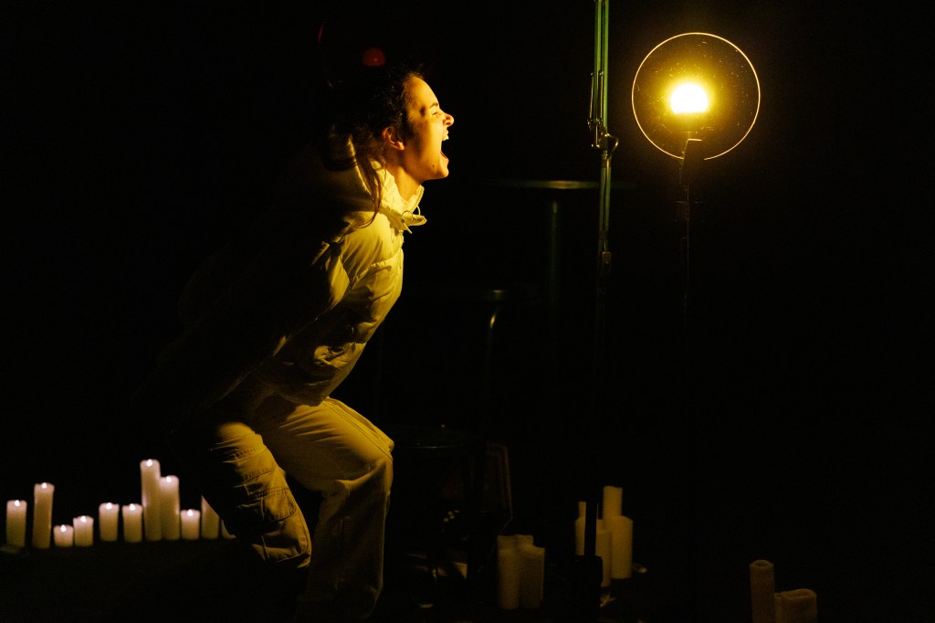 Cast member Katie Cherry, in all white screaming into the darkness with a dim yellow light in the background.