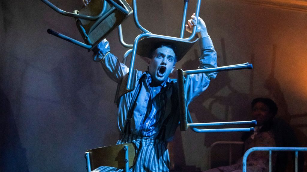 Photo shows Gregor (Felipe Pacheco) tied up with his whole body linked in chairs.